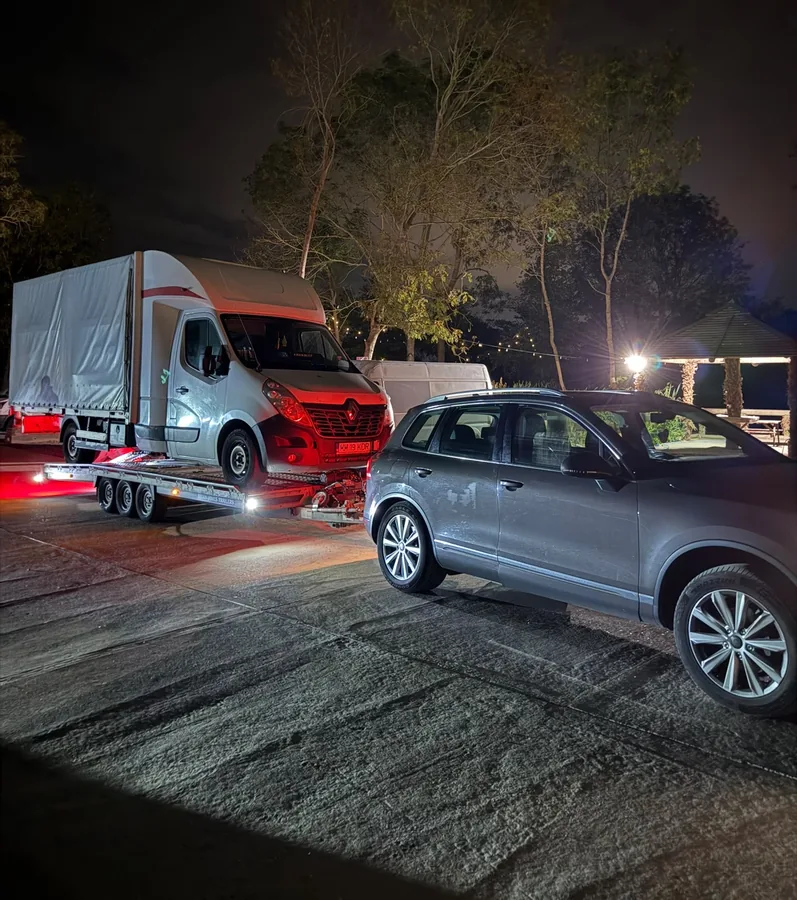 KCS Recovery transporter loaded with a box van under lights at night